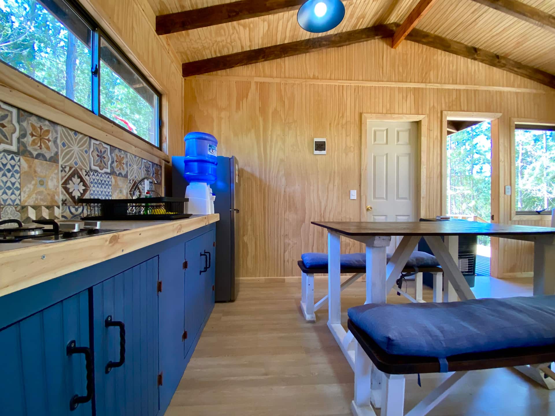 Cocina equipada con azulejos, refrigerador, bidón de agua filtrada y la mesa de comedor con bancas