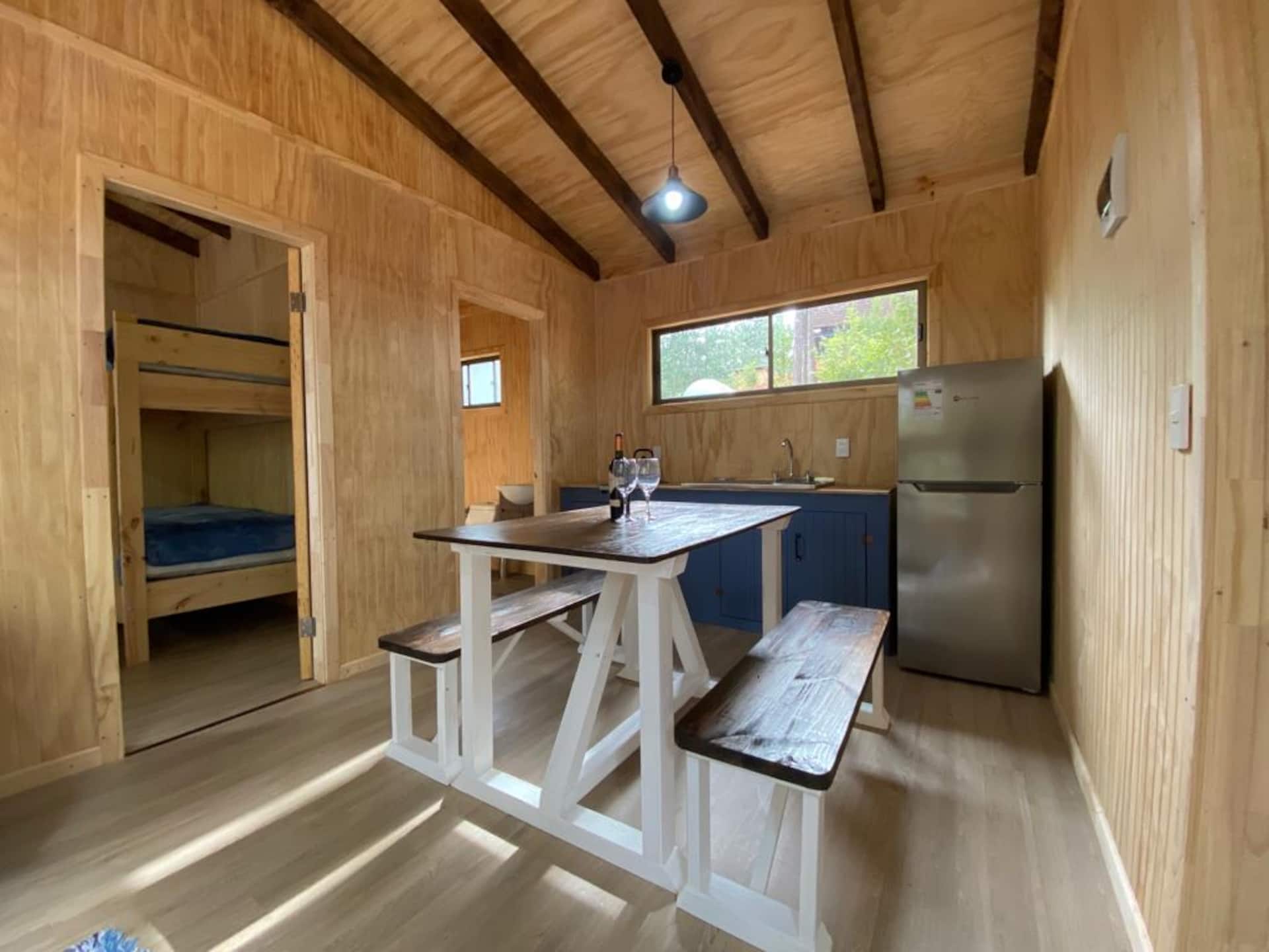 Comedor de madera en el centro de la cabaña, con la puerta abierta hacia la segunda habitación