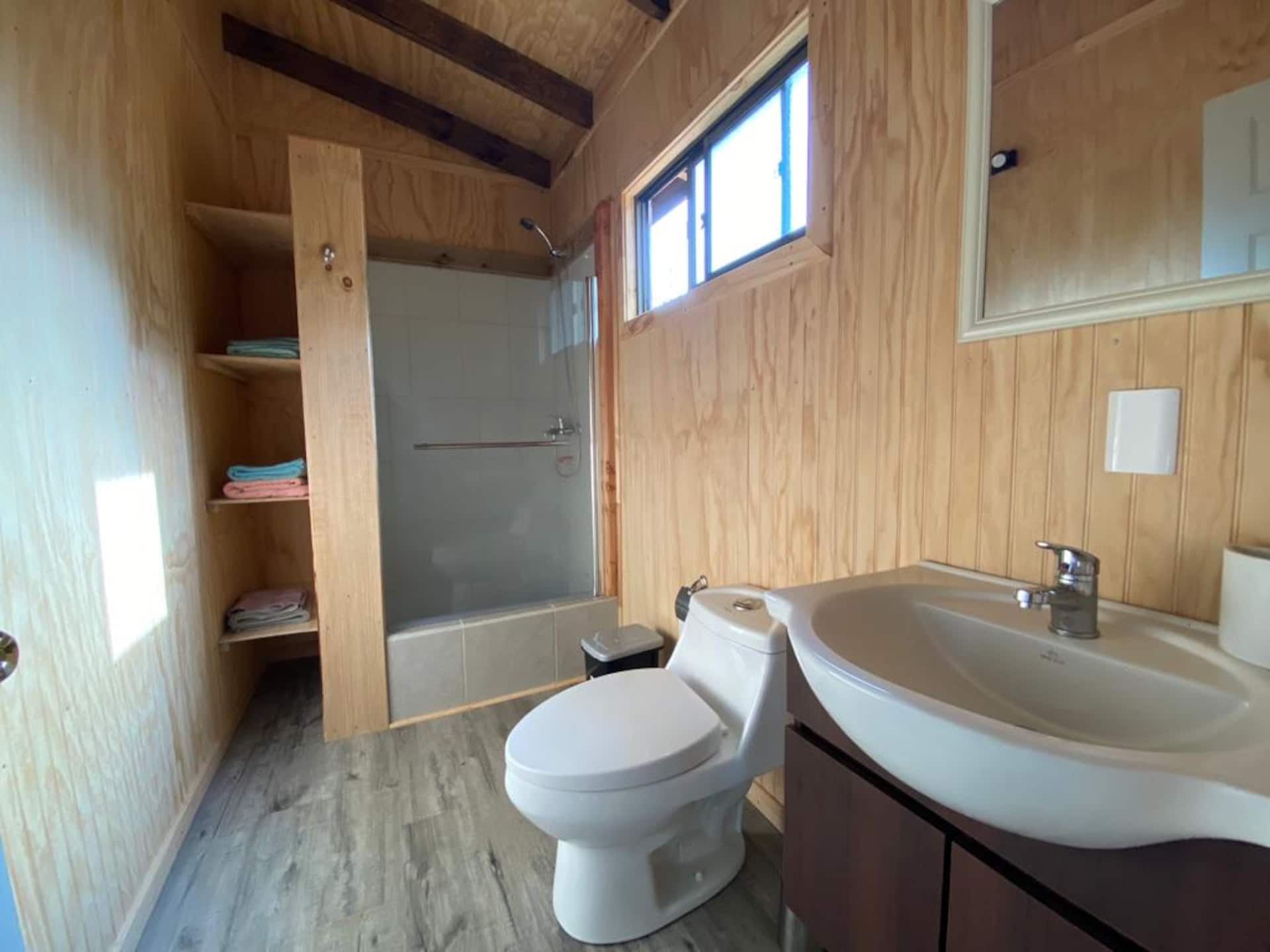 Baño con tina y ducha, lavamanos y repisas con toallas dobladas